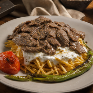 Yoğurtlu kızarmış patates üzerine sotelenmiş bonfile dilimleri, ızgara domates ve biberle servis edilmiş çeltik kebabı