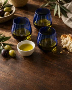 Kobalt mavisi tadım bardaklarında üç natürel sızma zeytinyağı, zeytin dalları ve ekmek