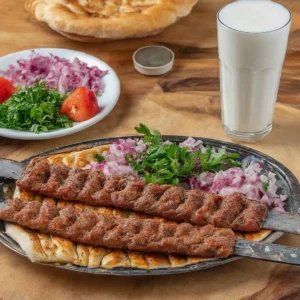 Pide üzerinde iki şiş Adana kebabı ve yanında doğranmış soğanla yeşillikler