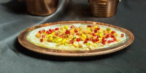 Bakır renkli tabakta nar taneleri ve kuruyemişlerle süslenmiş güllaç